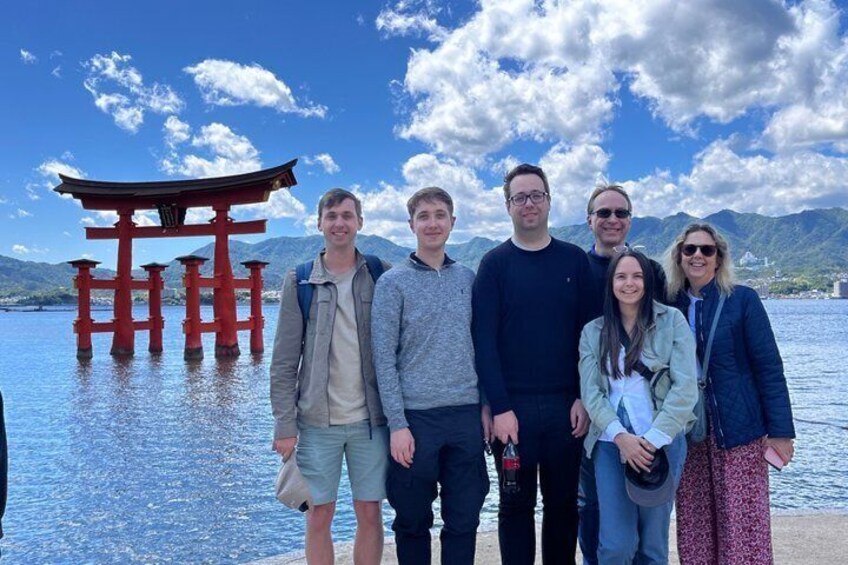 A group of people standing by a lake with a red torii gate in the background. 4
