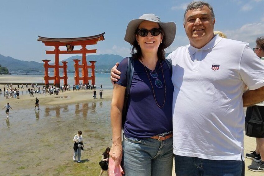A couple standing in front of a red torii gate with a beach and mountains in the background. 2