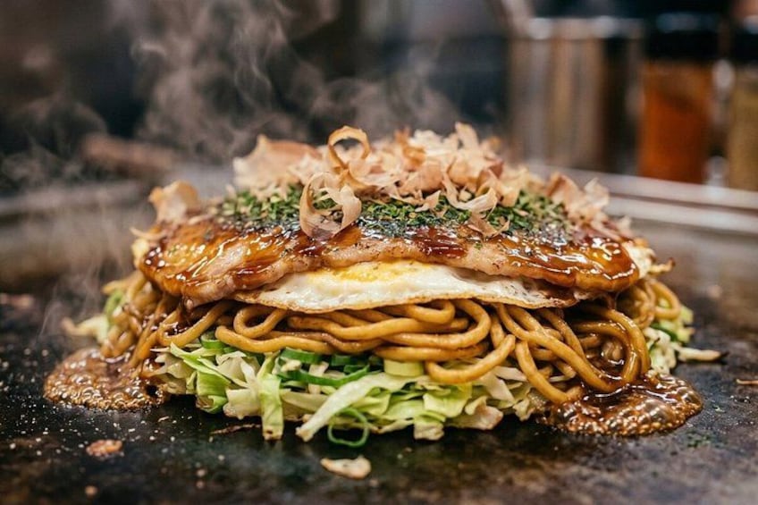 Un plato de fideos salteados cubierto con un huevo frito, adornado con cebolletas y semillas de sésamo. 2