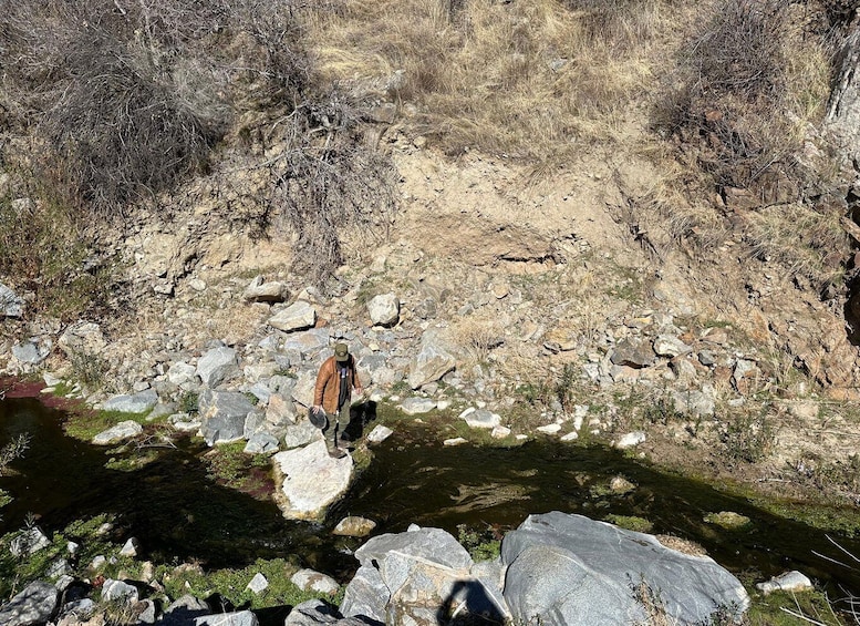 A hiker walking along a rocky stream with sparse vegetation. 3