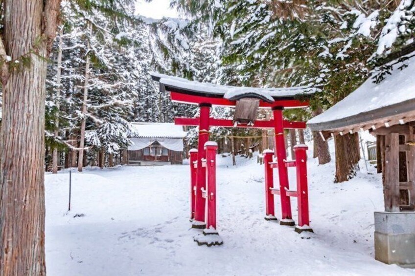 A red torii gate in a snowy forest with a cabin in the background. 3