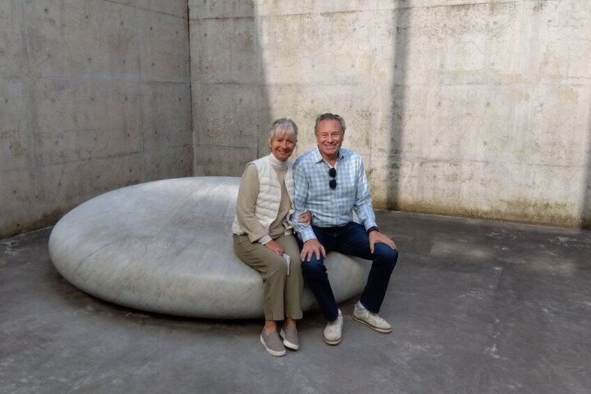 Two people sitting on a large, oval-shaped concrete structure in an indoor setting. 4