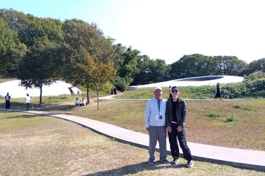 Dos personas están sobre un sendero en un parque con árboles y una estructura blanca al fondo. 2