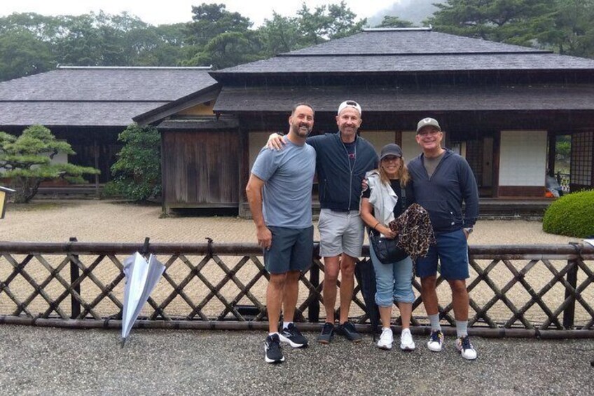 A group of people standing in front of a traditional Japanese building with a wooden fence in the foreground. 2