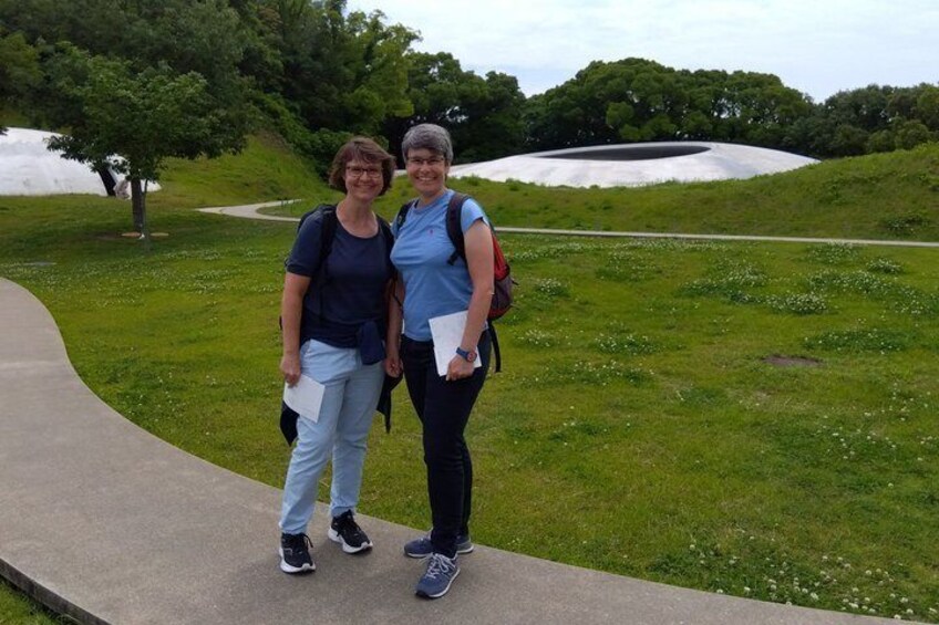 Two people standing on a concrete path with a grassy area and trees in the background. 5