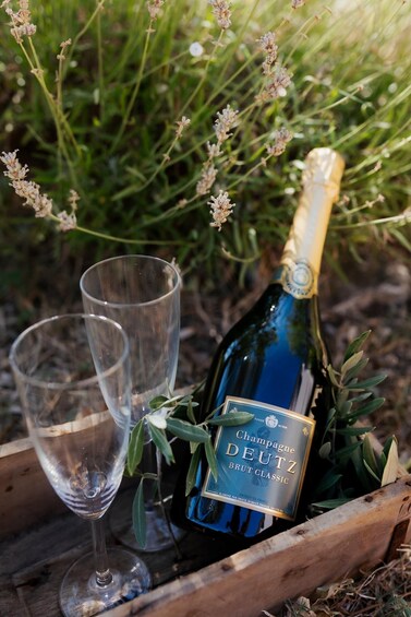 A bottle of Champagne Deutz Brut Classic with two empty glasses in a wooden crate. 4