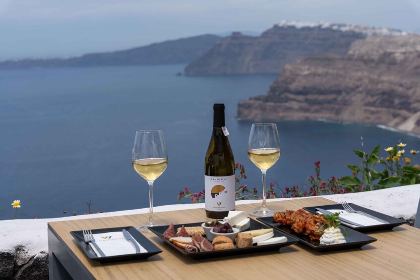 A table with a bottle of wine, two glasses, and a variety of cheeses and meats. 2