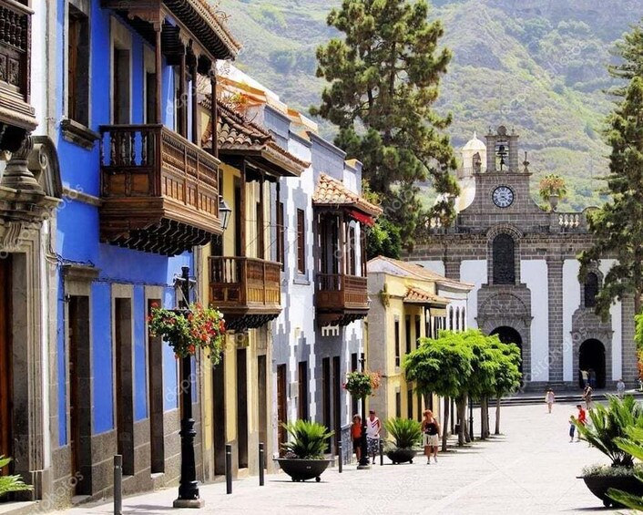 A historic street with colonial architecture, a clock tower, and lush greenery. 1