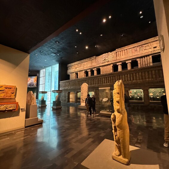 A museum interior with stone carvings, sculptures, and a large, illuminated wall. 2