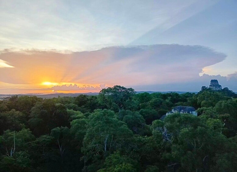 A sunset over a forested area with a prominent ancient pyramid structure. 3