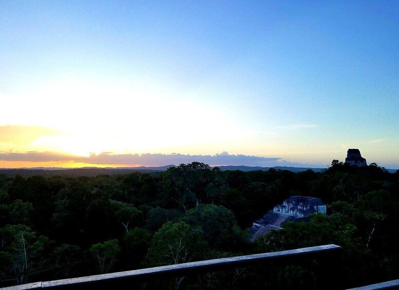 A sunset over a forested landscape with a pyramid-like structure in the distance. 4
