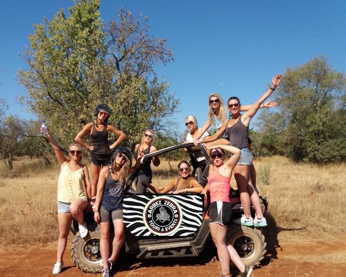 A group of people on a safari vehicle with a zebra design, surrounded by dry grass and trees. 2