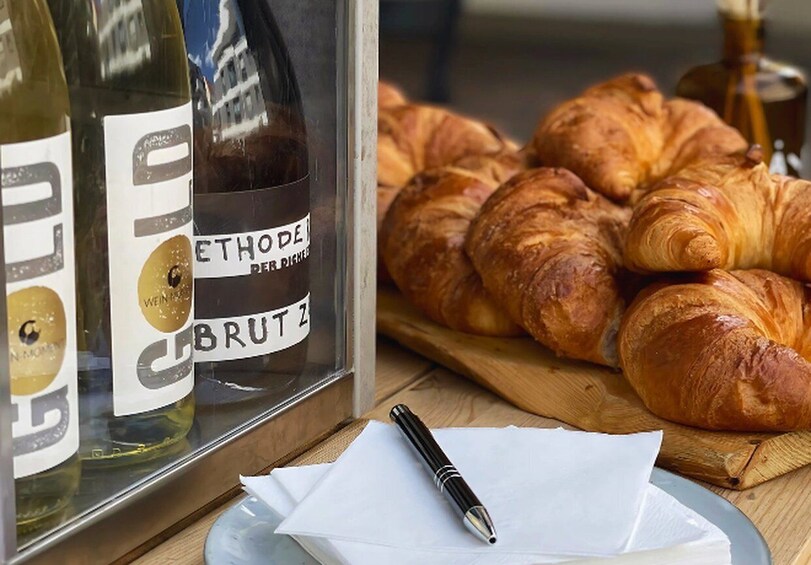 Bottles of wine, a pen, and croissants on a table. 3