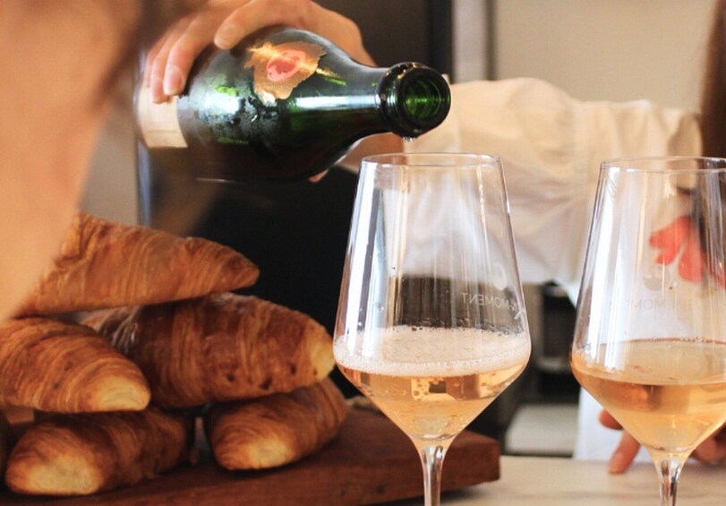 A person pouring a drink into a glass, with croissants in the background. 3