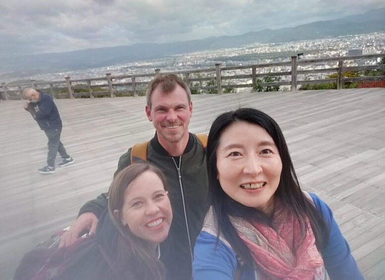 Three people taking a selfie on a wooden boardwalk with a cityscape and mountains in the background. 1