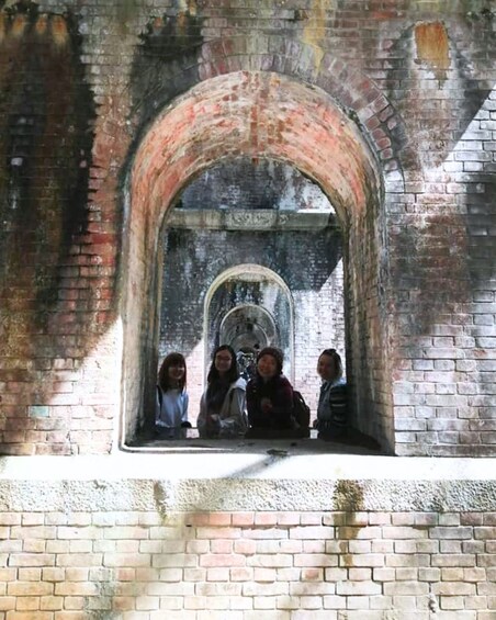 An arched window with a group of people inside, a brick wall, and a circular window below. 3