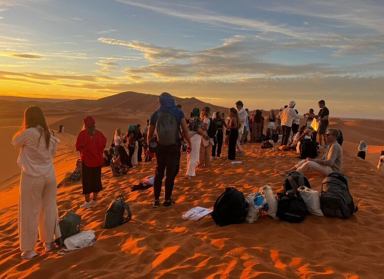 Un gruppo di persone riunite su una duna di sabbia nel deserto al tramonto. 5