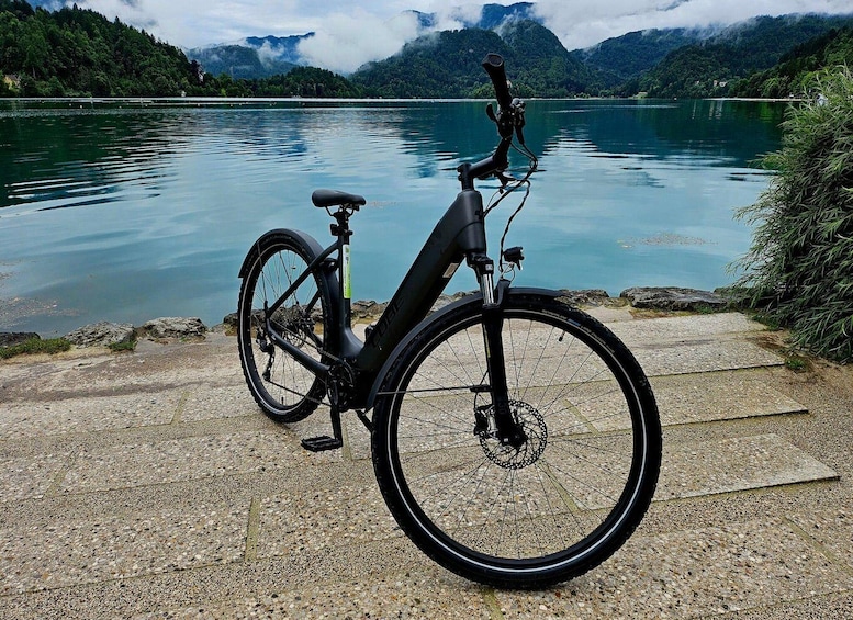 A stationary electric bike parked on a gravel path by a calm lake with mountains in the background. 1