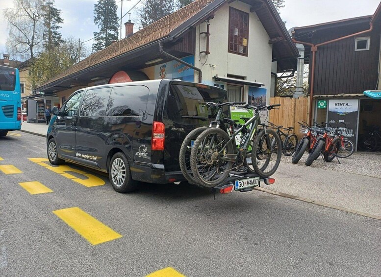 A black van parked on a street with yellow directional arrows, a building with a sign 'RENT A...', and bicycles mounted on the van. 2