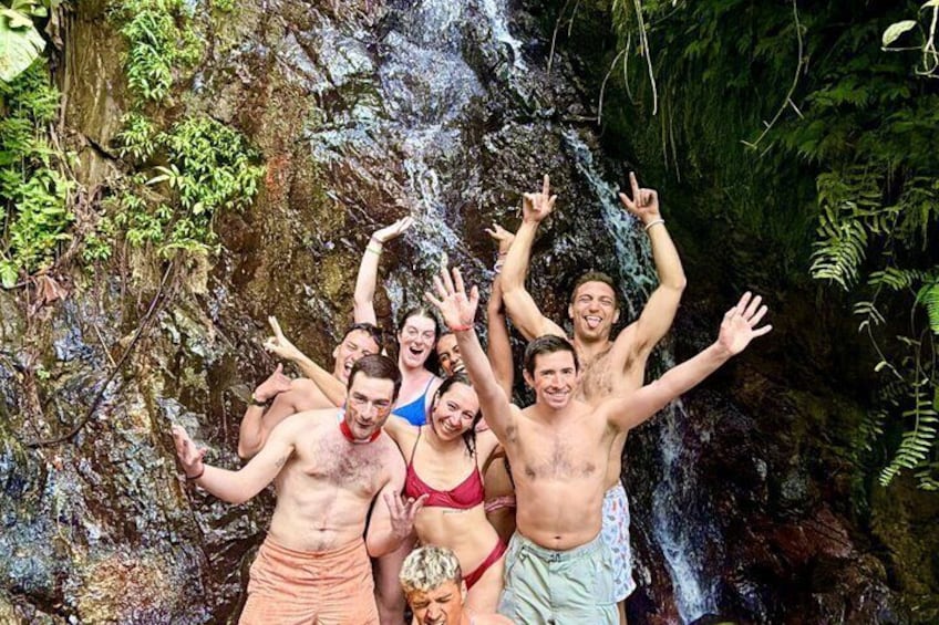 A group of people standing in front of a waterfall in a forested area. 1
