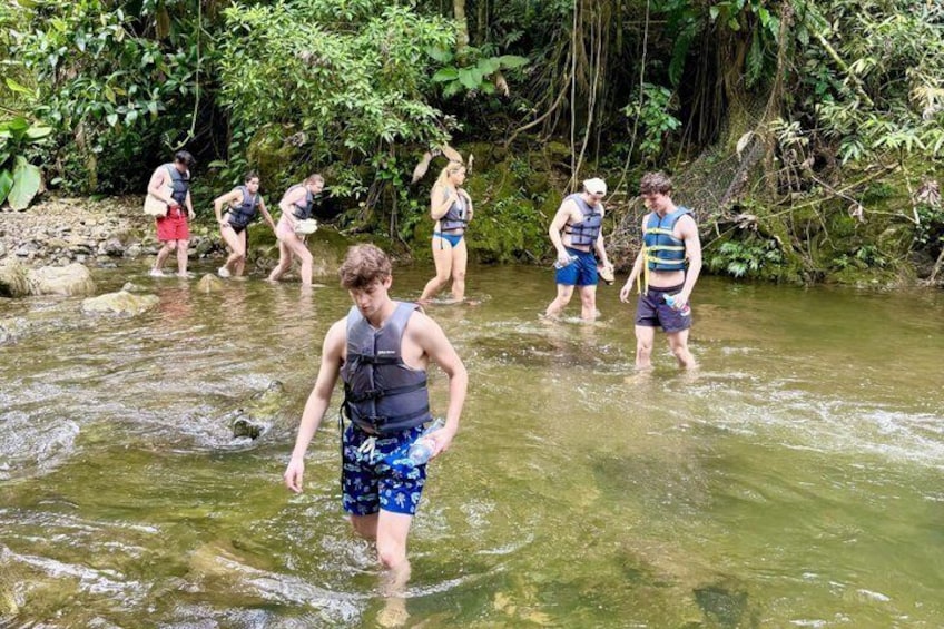 People wading through a shallow river surrounded by dense greenery. 2