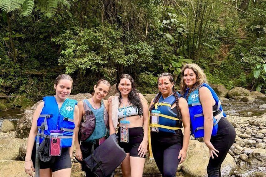 Five people wearing life jackets, standing on rocks by a stream in a forested area. 5