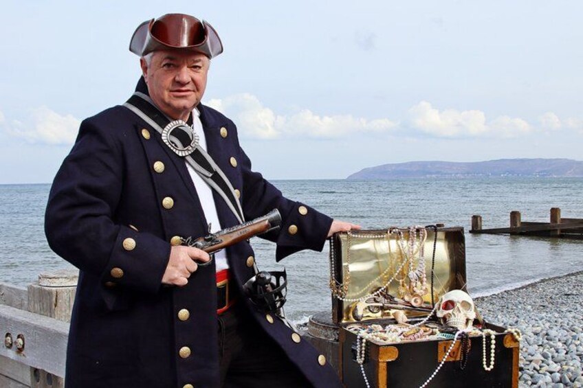 A person in a pirate costume holding a pistol, standing next to an open treasure chest filled with gold coins and jewels. 5