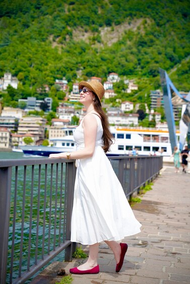 A woman in a white dress and red shoes standing by a river, overlooking a city with buildings and a bridge. 4