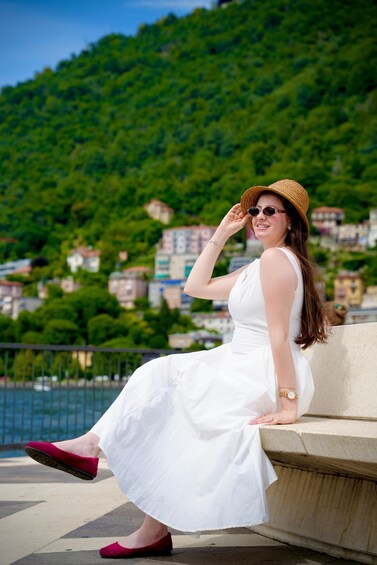 A person in a white dress sitting on steps with a green hillside and buildings in the background. 3