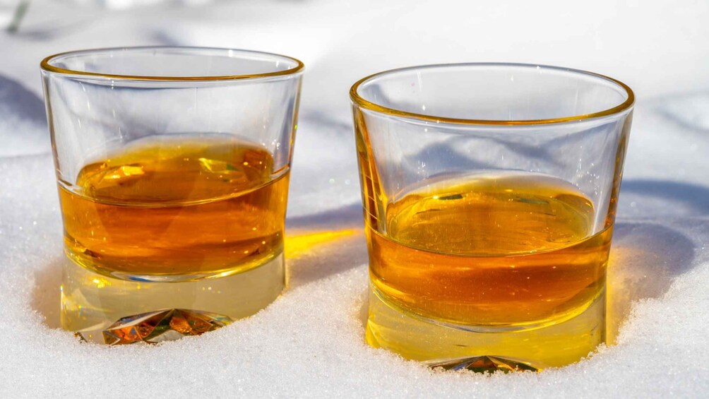 Two glasses of amber liquid on a snowy surface. 4