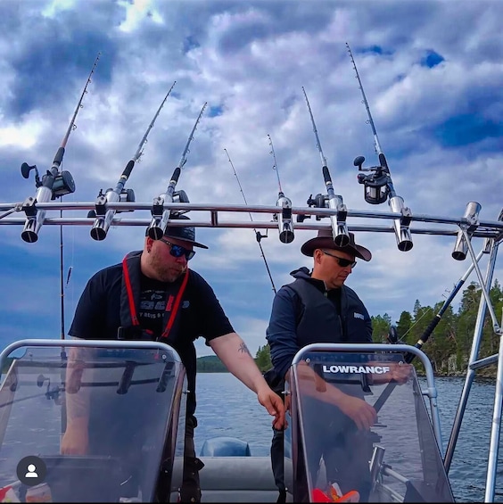 Two people on a boat with multiple fishing rods mounted on a rail. 1