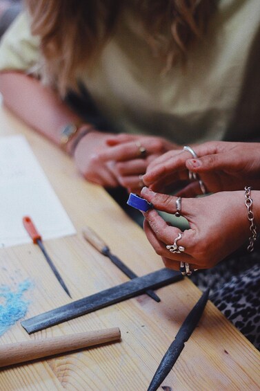 Hands holding a small object, possibly a tool, with a wooden surface and various items like pencils and a ruler. 1
