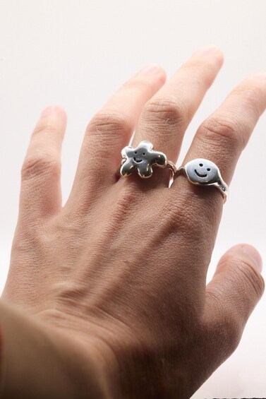 A hand with two rings, one shaped like a bear and the other a smiley face. 3