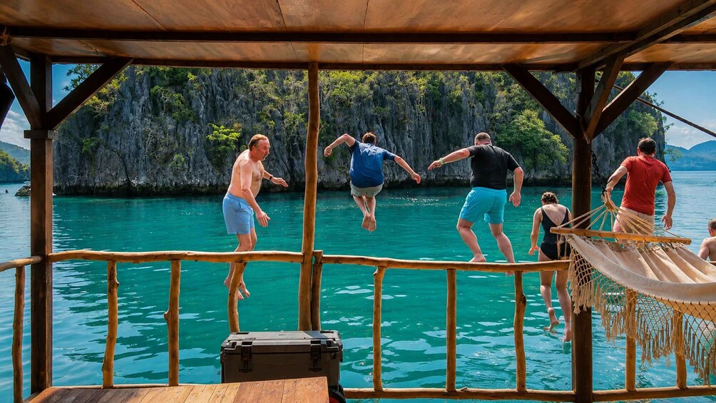 People jumping off a dock into turquoise water with a rocky landscape in the background. 5