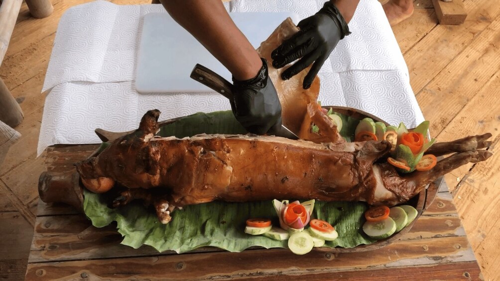 A roasted pig on a wooden table with a white cloth, surrounded by sliced vegetables. 3