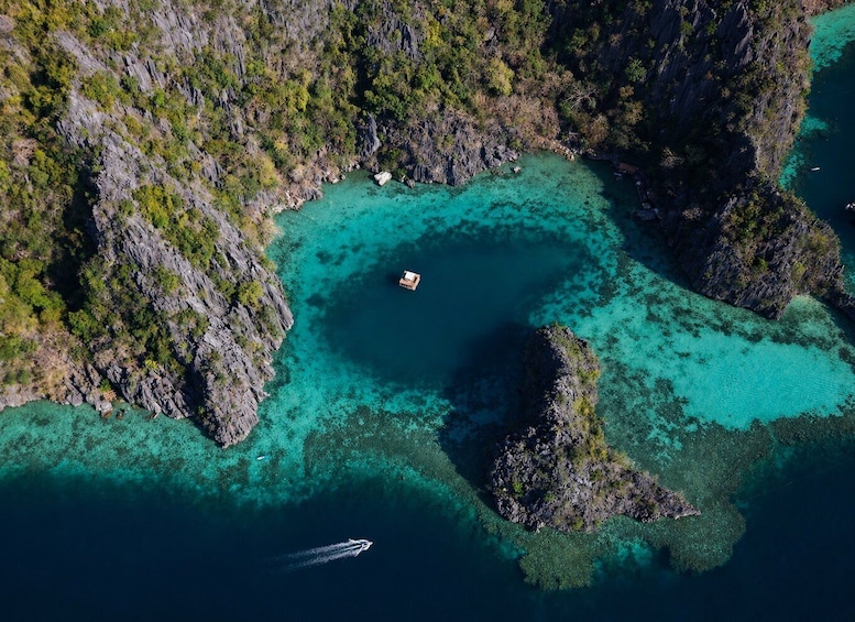 An aerial view of a coastal area with clear turquoise waters, rocky outcrops, and a small boat anchored near the shore. 1