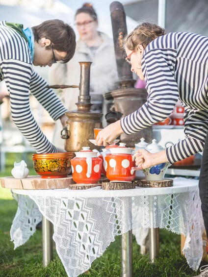 Two people serving tea from red teapots with white polka dots on a table with a lace tablecloth. 4