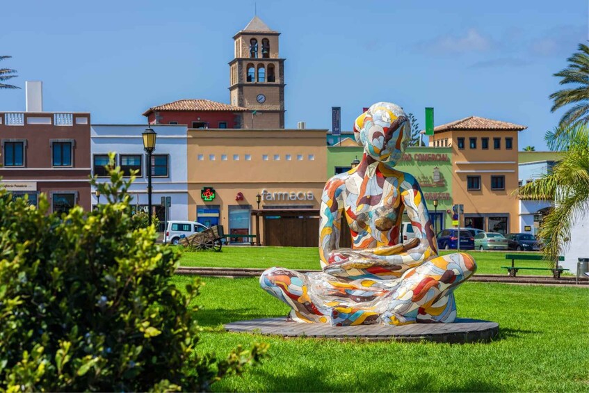 A colorful abstract sculpture in a public square with buildings and a clock tower in the background. 1
