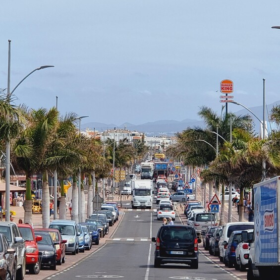 A busy urban street lined with parked cars, palm trees, and a Burger King sign. 5