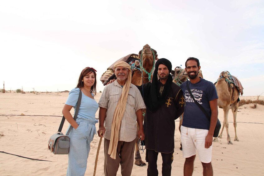 A group of people standing in a desert with camels in the background. 2
