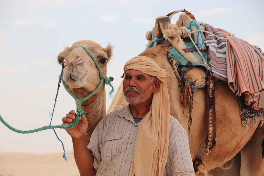 A man holding a camel's rope, with a camel and a desert landscape in the background. 3