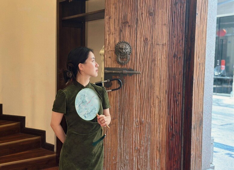 A person in a green dress standing at a wooden door with a brass knocker and a decorative metal plate. 3