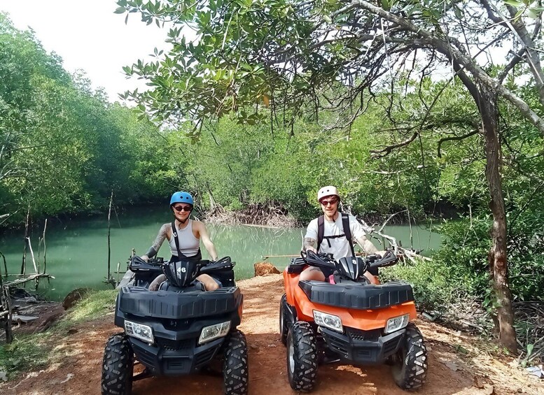 Two people on all-terrain vehicles in a forested area with a body of water. 3