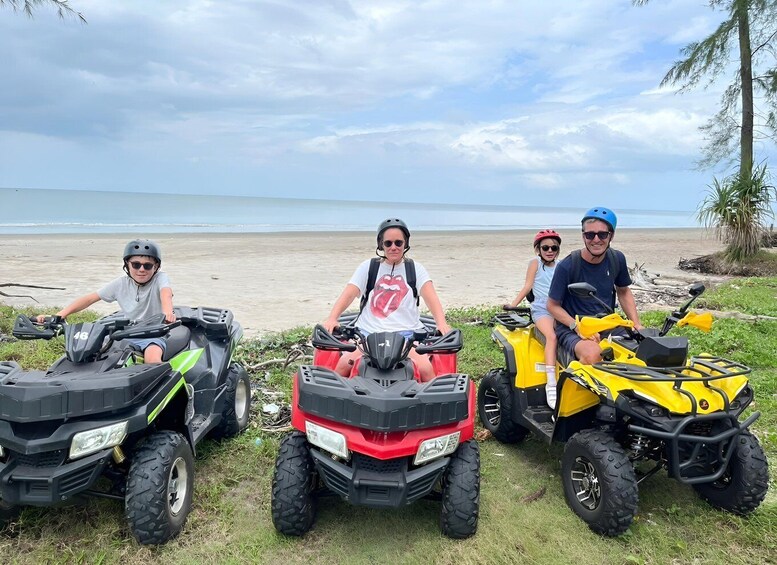 Four people on all-terrain vehicles (ATVs) on a beach with the ocean in the background. 1