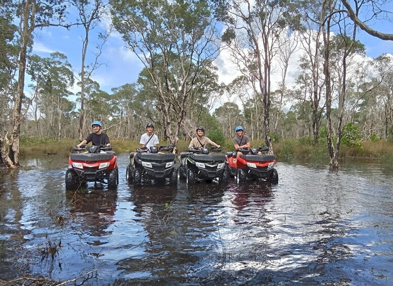 Four people on all-terrain vehicles in a flooded area with trees. 5