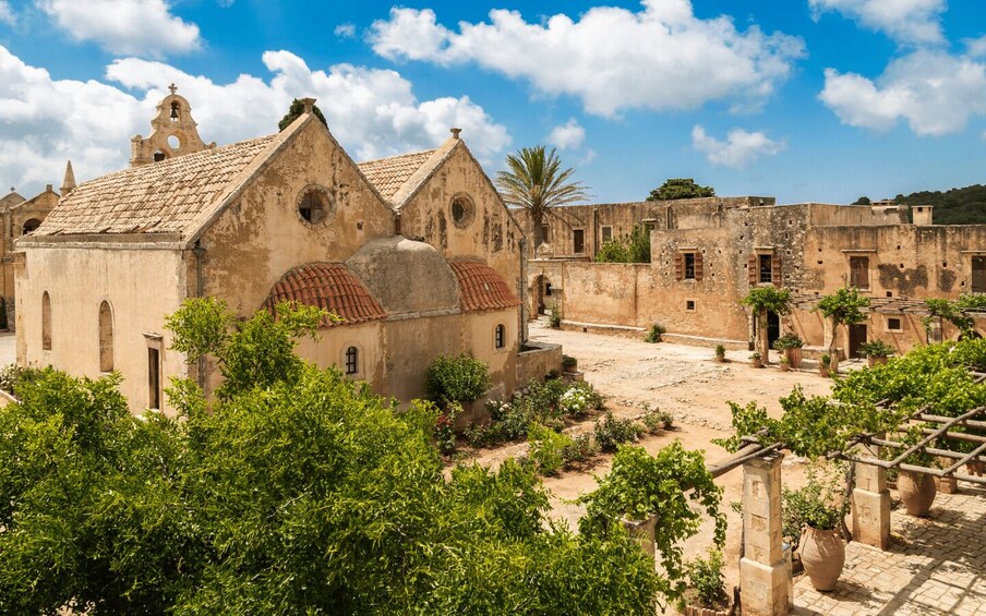 An old courtyard with historic buildings, including a church with a bell tower, surrounded by greenery. 5
