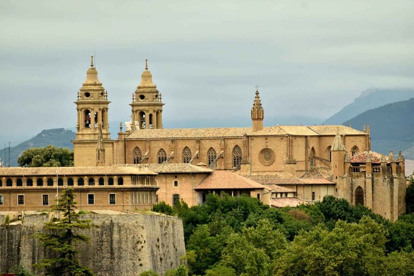 A historic church with two bell towers, surrounded by lush greenery and mountains in the background. 1