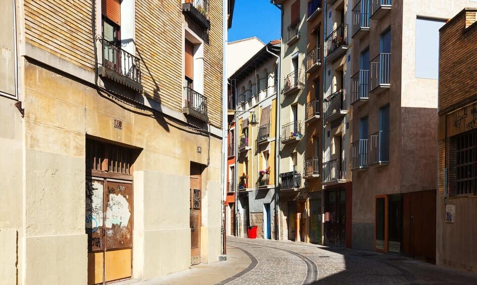 A narrow cobblestone street flanked by multi-story buildings with balconies and windows. 2