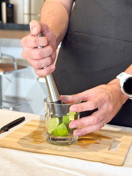 A person using a metal tool to crush lime in a glass. 1