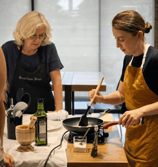 Two people cooking, one stirring a pan and the other standing by. 2